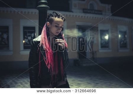 Portrait Of A Smoking Woman. A Woman With A Cigarette Stands At Night Near A Street Lamp. Informal M