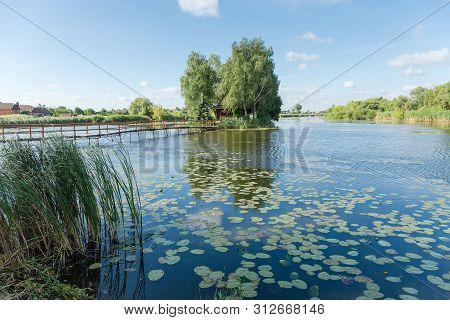 Tiny Island With Trees And Romantic Fishing Hut On Lake And Small Wooden Footbridge To Him In Summer