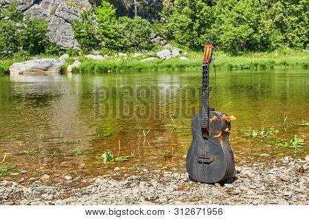 Burning Guitar On The Banks Of A Mountain River. Careless Handling Of Fire In Nature. Incendiary Jou