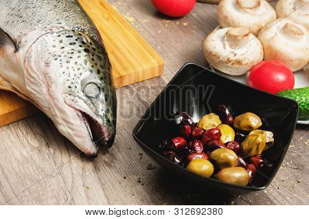 Close-up Keta Fish, Whole On The Cutting Board Of The Kitchen Table Next To Olives Tomatoes And Mush