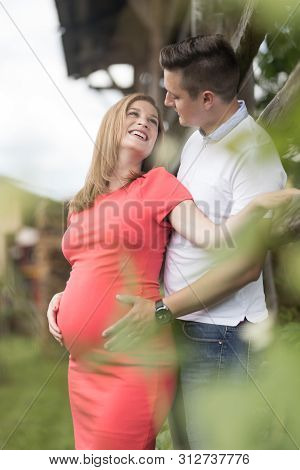 Young Happy Pregnant Couple Hugging At Countryside By Hayrack.