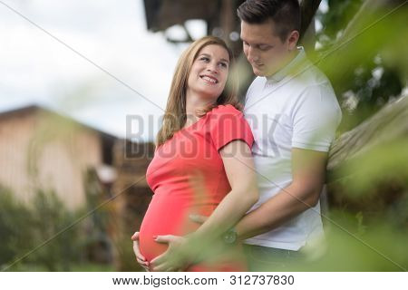 Young Happy Pregnant Couple Hugging At Countryside By Hayrack.