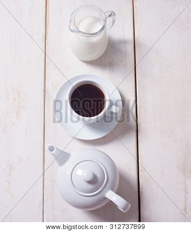 Cup Of Coffee, Teapot And Jug With Milk In Row Over White Wooden Background. Flat Lay, Copy Space