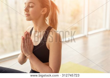 Young Female Clasping Hands And Closing Eyes While Meditating During Yoga Lesson In Gym