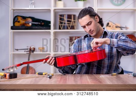 Young handsome repairman repairing guitar