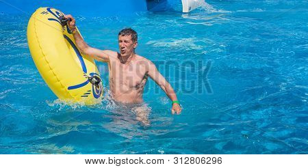 Retired But Still Active Man In His Sixties Getting Out Of Swimming Pool. Man Is Holding Yellow Infl
