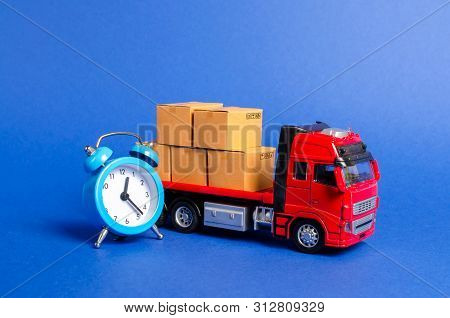 A Red Truck With Cardboard Boxes And A Blue Alarm Clock. Express Delivery In Short Time Concept. Tem