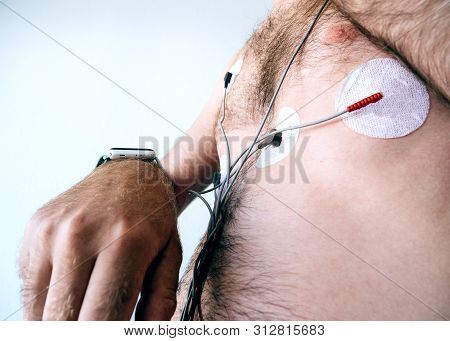 Side View Of Man Setting Smartwatch Wearing A Heart Monitor Holter Attached To Sensors Stuck To Ches