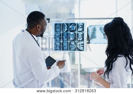 Two Doctors Are Looking At X-rays. Medical. Rear View Of Chief Physician Afro American Man And Cauca
