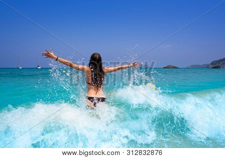 Ibiza beach girl splashing water open arms in Balearic islands