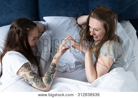 Two Smiling Lesbians Touching Hands And Looking At Each Other In Bed