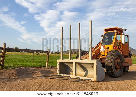 Side Angle Of Orange Tractor With A Plow In A Field With Blue Sky In The Background