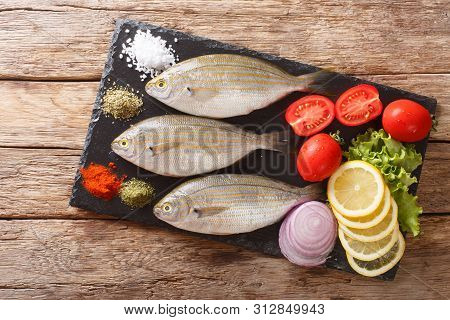 Preparation For Cooking Sarpa Salpa Fish With Lemon, Vegetables And Spices Close-up On A Slate Board