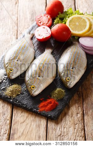 Preparation For Cooking Sarpa Salpa Fish With Lemon, Vegetables And Spices Close-up On A Slate Board