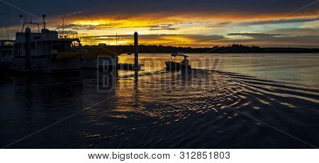 A Striking Inspirational Golden Colored Cloudy Marina/dock Sunset Seascape Over Sea Water With Water