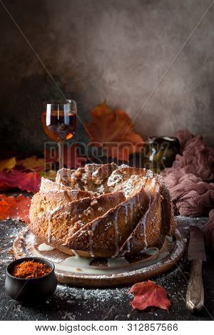 Bundt Cake With Saffron And Rum Covered With White Glaze On Rustic Background With Autumn Decoration