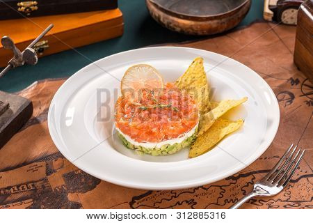 Tartar With Salmon, Avocado, Cream Cheese And Nachos On White Plate On Old Map Background Side View