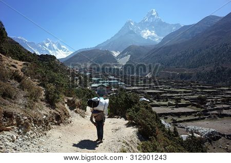 Porter carries heavy load near Pangboche village with view of mount Ama Dablam