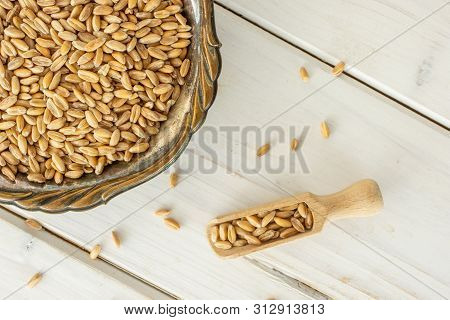 Lot Of Whole Fresh Beige Dinkel Wheat Grain In Old Iron Bowl With Wooden Scoop Flatlay On White Wood