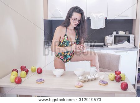 Happy Woman In Fashionable Swimsuit With Green Leaves Posing In White Kitchen