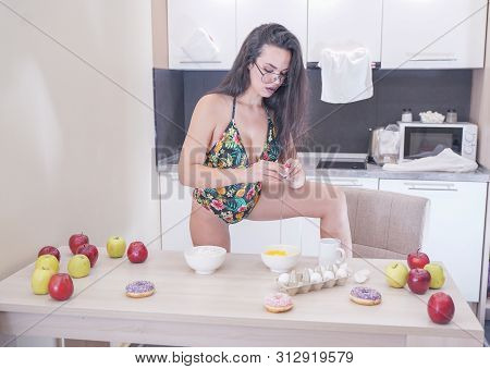Happy Woman In Fashionable Swimsuit With Green Leaves Posing In White Kitchen