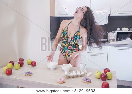 Happy Woman In Fashionable Swimsuit With Green Leaves Posing In White Kitchen