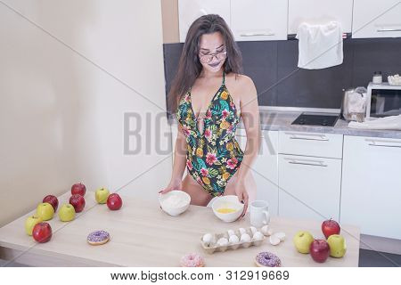 Happy Woman In Fashionable Swimsuit With Green Leaves Posing In White Kitchen