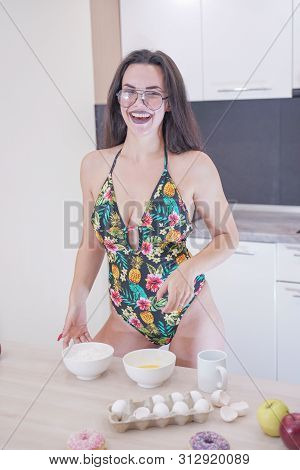 Happy Woman In Fashionable Swimsuit With Green Leaves Posing In White Kitchen