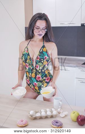 Happy Woman In Fashionable Swimsuit With Green Leaves Posing In White Kitchen