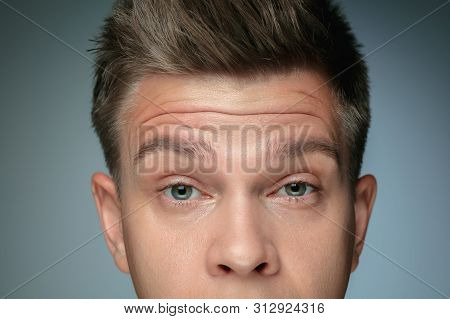 Close-up Portrait Of Young Man Isolated On Grey Studio Background. Male Face With Wrinkless. Concept