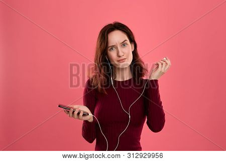 Portrait Of A Pretty Brunette Girl Holding Earphone In One Hand And Mobile Phone In Another One Expr