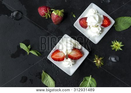 Fresh Strawberries With Whipped Cream On A Black Background, Pieces Of Strawberries And Whole Berrie