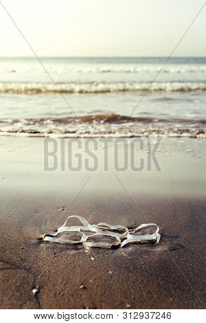 Vertical Background Of A Plastic Rings Lying On The Shore Of The Beach And Pollutes The Sea And The 