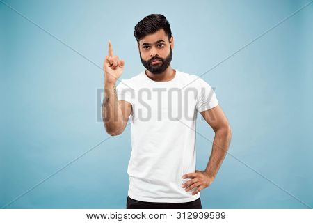 Half-length Close Up Portrait Of Young Hindoo Man In White Shirt On Blue Background. Human Emotions,