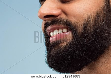 Close Up Portrait Of Young Hindoo Mans Face With Beard, White Teeth And Lips On Blue Background. Smi