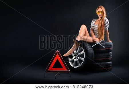 Tires And Girl. Girl In Protective Glasses With Wrench Sitting On Tires.