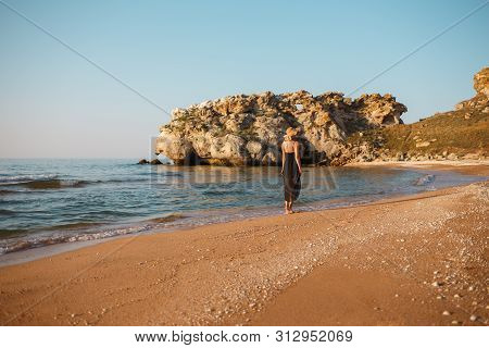 Portrait Of A Girl In A Black Dress And Hat On The Beach