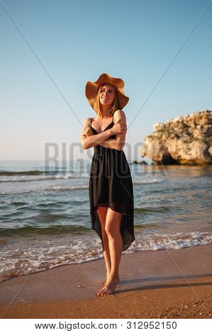 Portrait Of A Girl In A Black Dress And Hat On The Beach