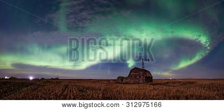 Swirl Of Bright Northern Lights Over Vintage Barn, Bins, Windmill And Stubble In Saskatchewan, Canad