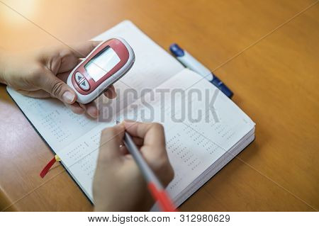 Close Up Of Woman Hands Holding Glucose Meter And Use Pen To Write Schedule Check Blood Sugar Level 
