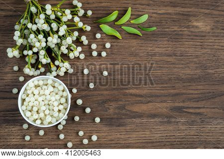 Container With Mistletoe Fruit And Branches Of Evergreen White Mistletoe On A Wooden Surface, Top Vi