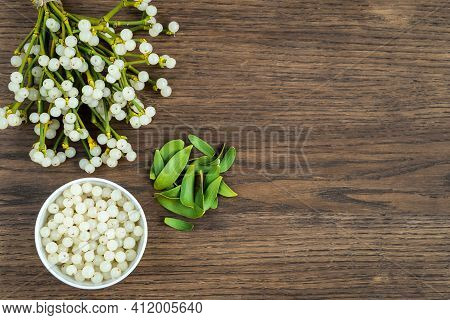 Container With Mistletoe Fruit And Branches Of Evergreen White Mistletoe On A Wooden Surface, Top Vi