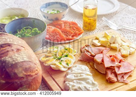 Continental, healthy breakfast containing homemade bread, vegetables tomatoes, argula, sald, cheese burratta, camembert, ham and egg. 