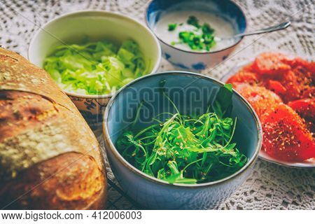 Vegetarian healthy breakfast containing homemade bread, vegetables tomatoes, argula with sesame seed, sald, iceberg lettuce and garlic sauce with chives