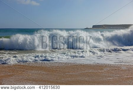 Waves Crashing Onto A Sandy Beach In The Algarve