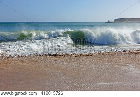 Waves Crashing Onto A Sandy Beach In The Algarve