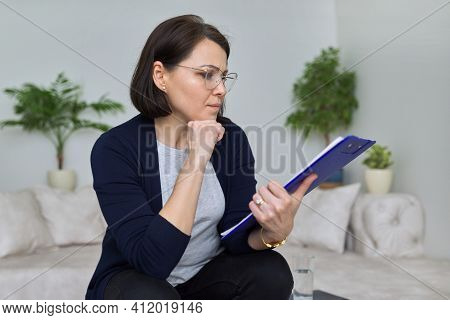 Serious Mature Business Woman With Glasses Reading Paper Files.