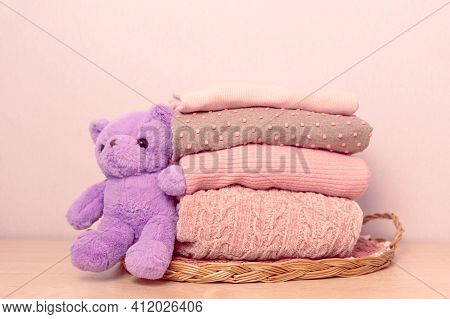 Stack Of Folded Wool Knitted Sweaters Or Pullovers In Pink Pastel Colors On Table With Soft Toy Tadd