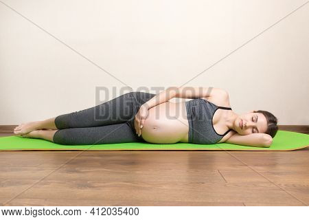 Beautiful Young Pregnant Woman Sitting On Mat In Yoga Pose At The Home. Pregnancy Yoga And Fitness C