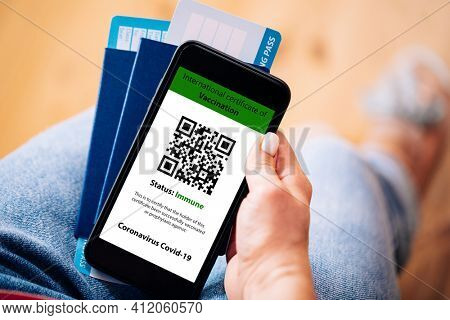 The woman holding the mobile phone a mockup for digital vaccination certificate in one hand and passport, mask and ticket in another one